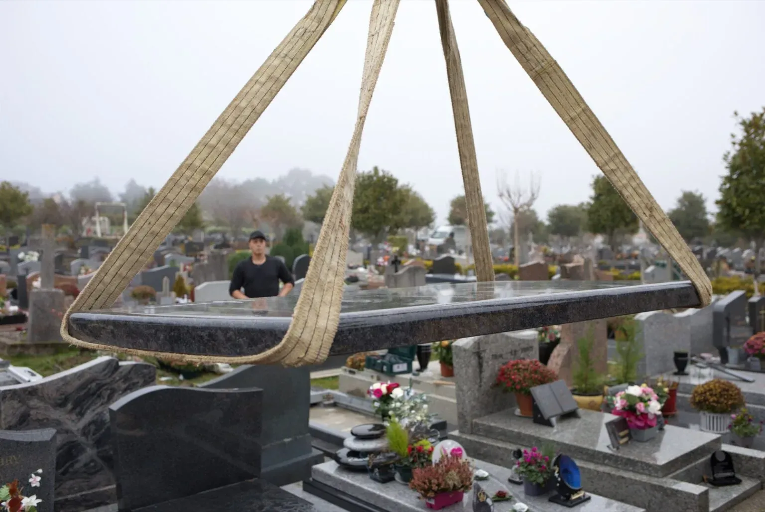 Pose et manutention d'une dalle funéraire en granit suspendue par des sangles dans un cimetière.