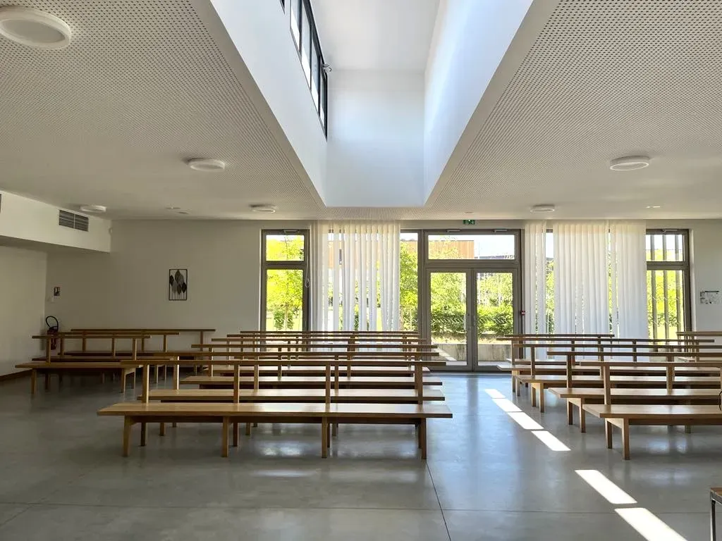 Grande salle de cérémonie lumineuse du crématorium avec bancs en bois.