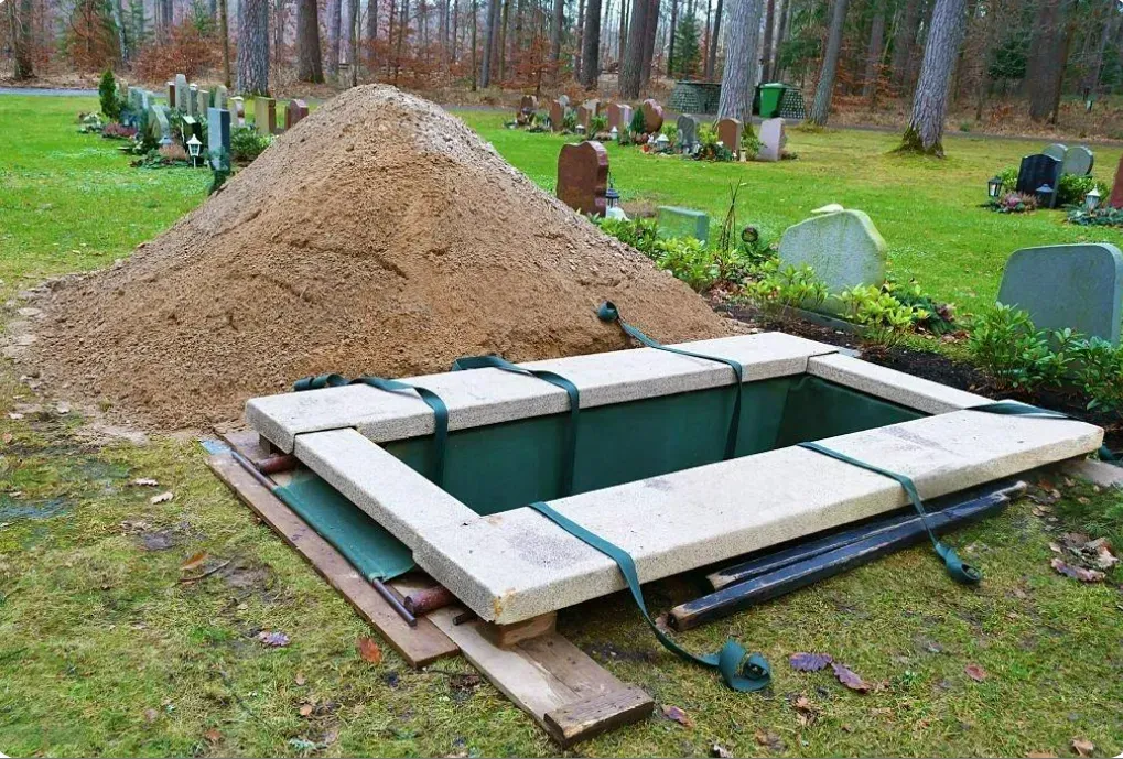 Fosse d'inhumation préparée avec sangles dans un cimetière paysager.