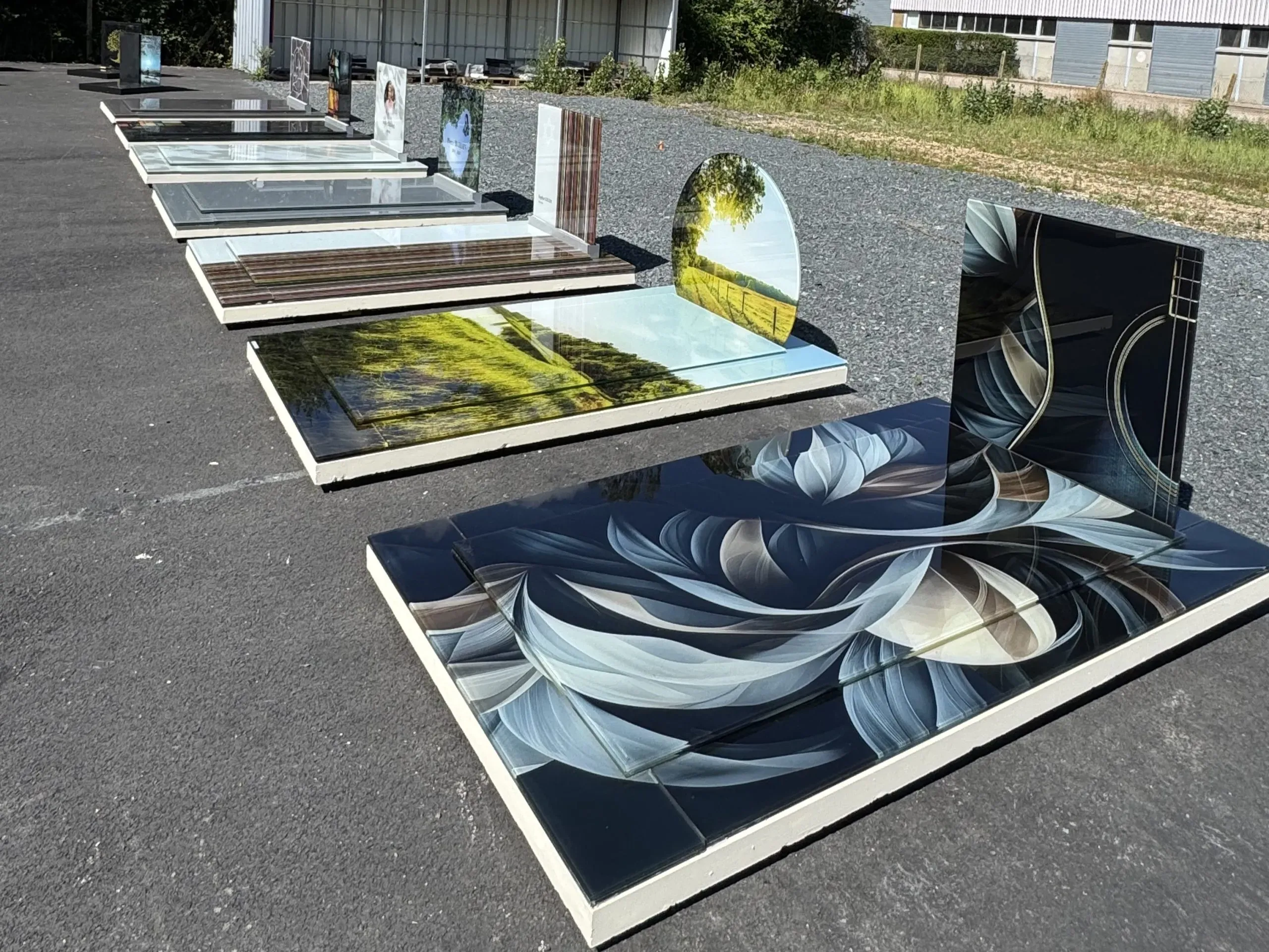 Alignement de monuments funéraires modernes en verre imprimé sur parc d'exposition.