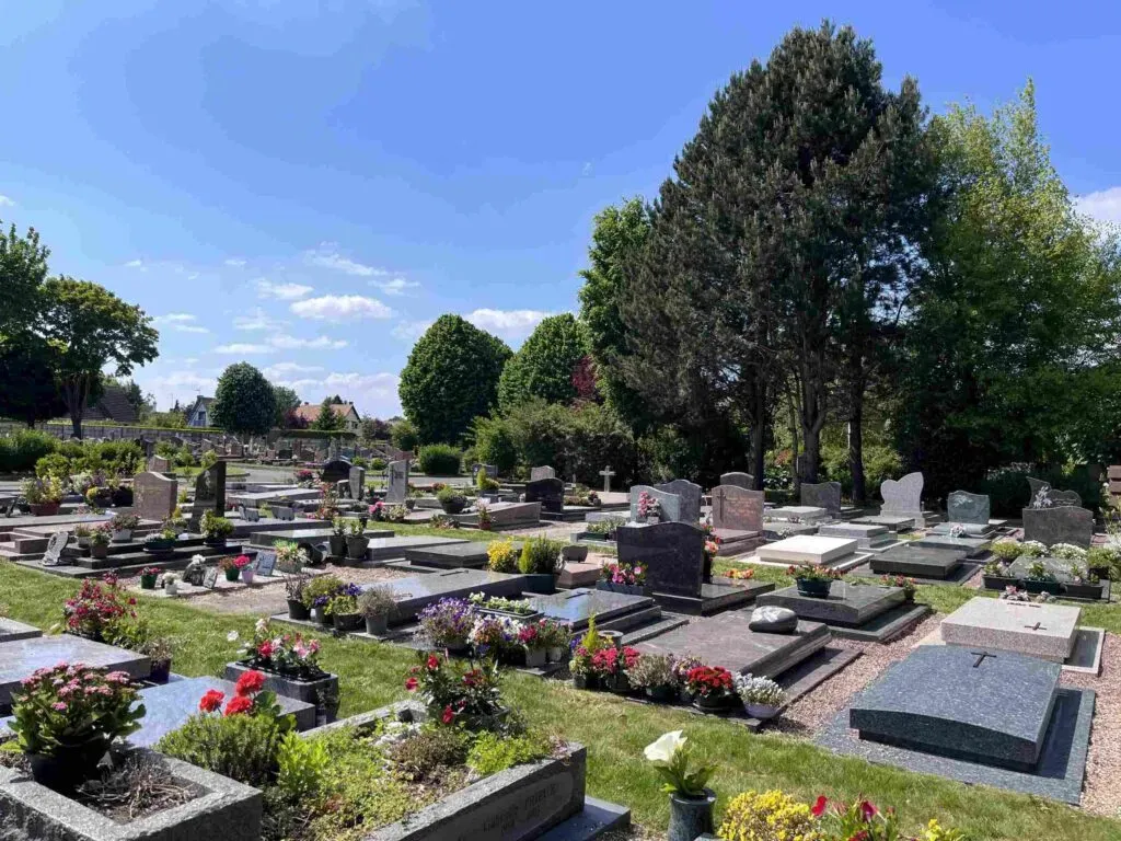 Vue d'ensemble d'un cimetière paysager avec tombes et parterres fleuris sous un ciel bleu.